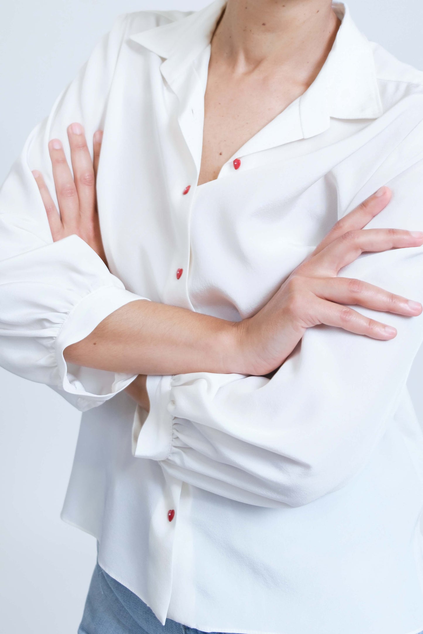Chemise femme réalisée à la main en crêpe de soie blanc et ses boutons coeur rouges, vue rapprochée de face, détail manches froncées et mancheron de bas de manche.