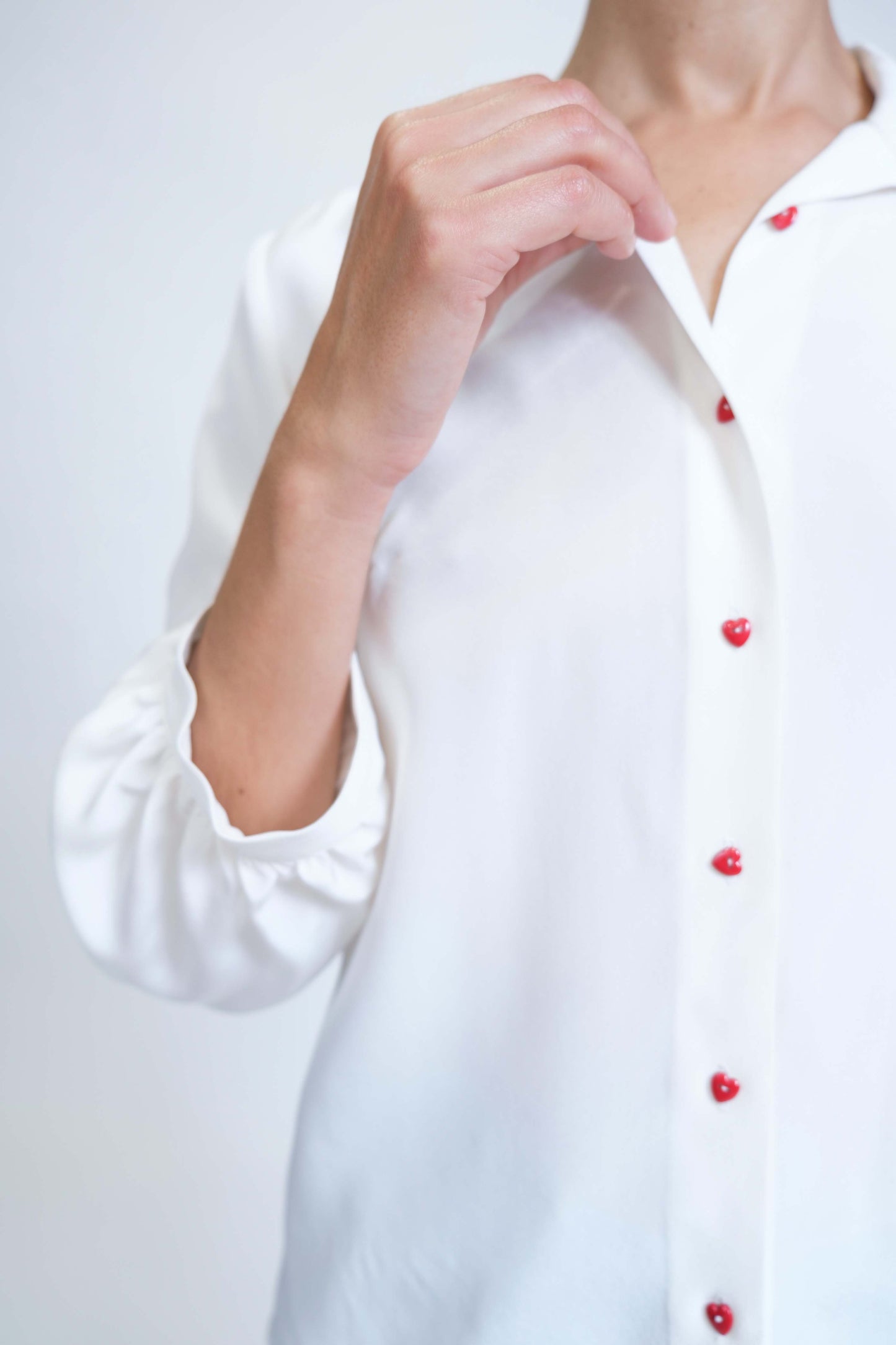 Chemise femme réalisée à la main en crêpe de soie blanc et ses boutons coeur rouges, vue rapprochée de face, détail patte de boutonnage et boutons coeur rouges.