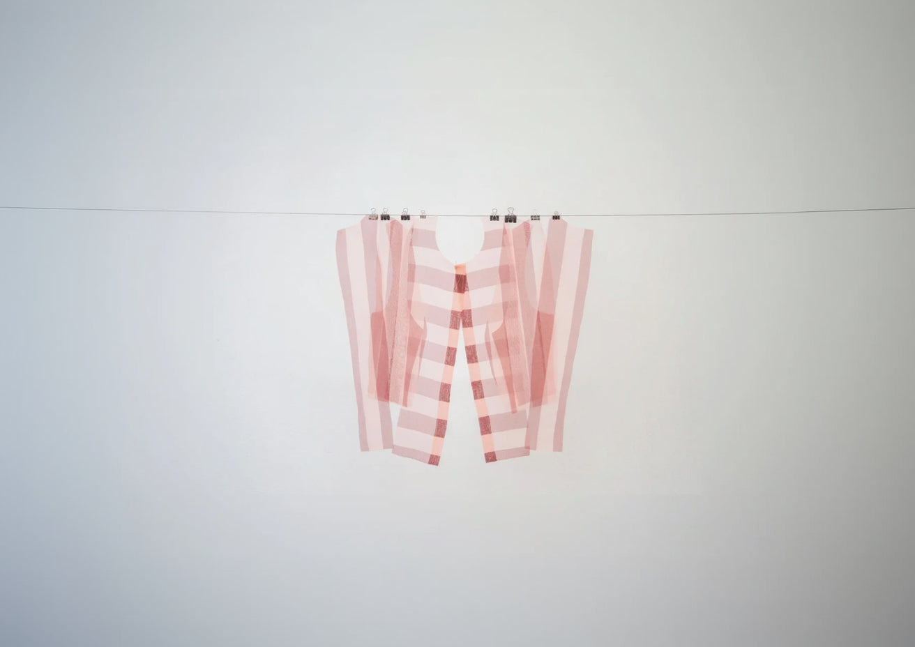 Pièces d'une chemise en organza rayé rose et bordeaux, suspendues à un fil. 