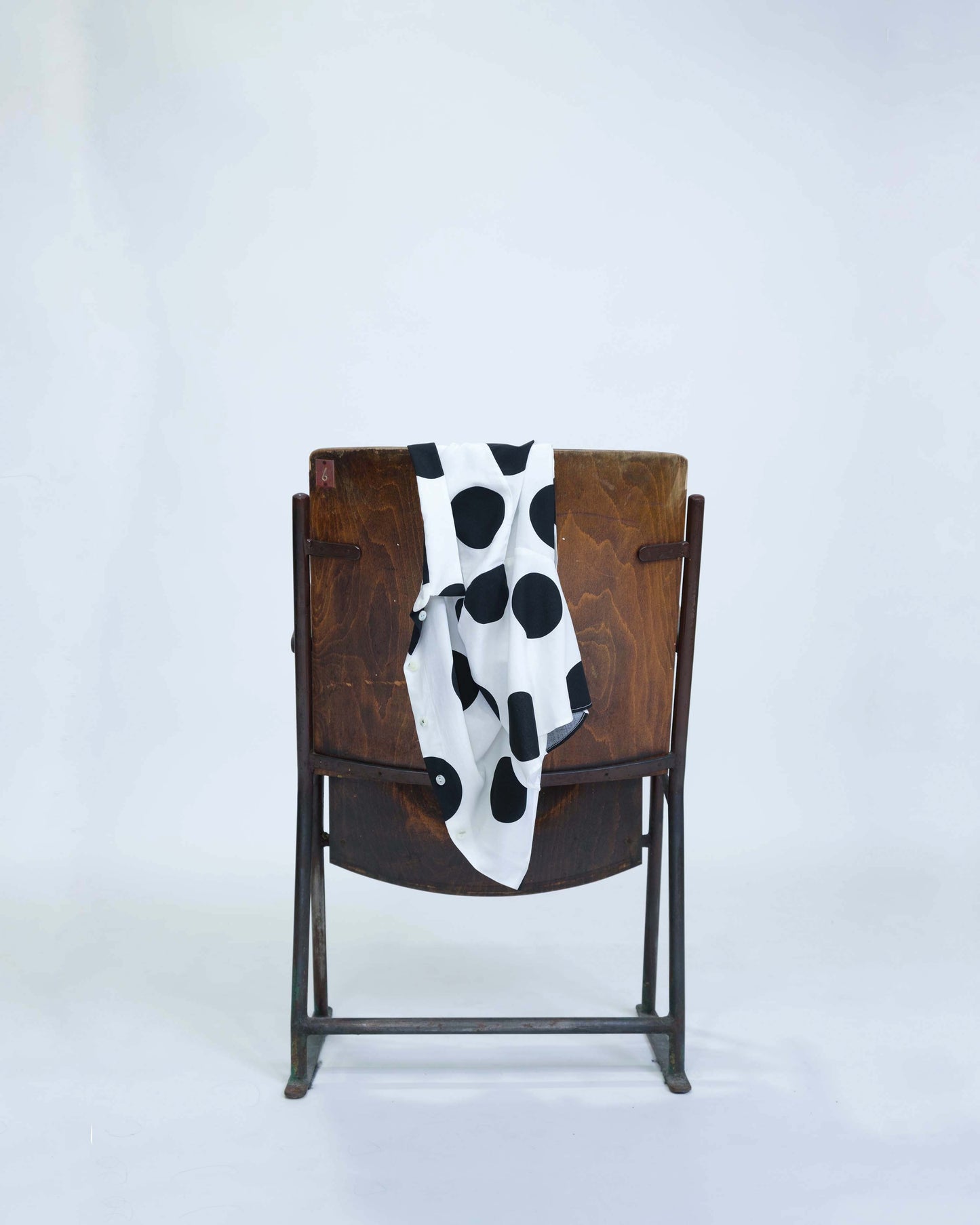 Chemisette pour femme réalisée à la main en deux exemplaires, en viscose blanche à gros pois noir, posée sur le dossier d'une chaise en bois, détail tombé du tissu. 